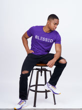 Load image into Gallery viewer, Model wearing purple shirt with Blessed written across the chest in white text. 

